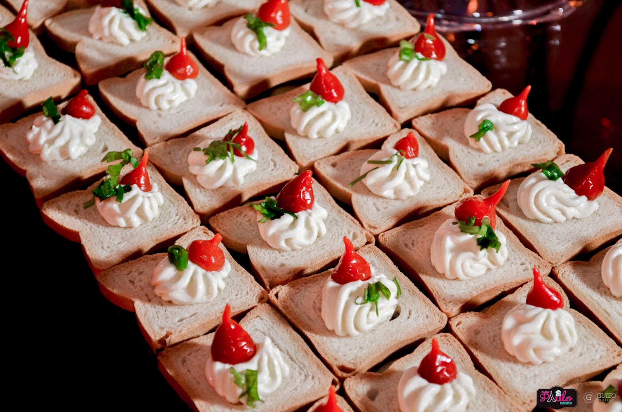 who-we-are Gourmet appetizers with cream cheese and red peppers on bread slices, perfect for parties or buffets.