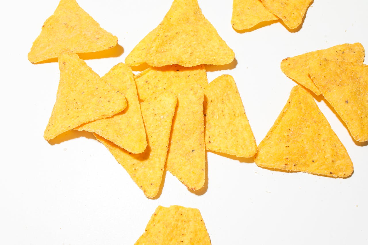 team-03 Close-up of crunchy yellow corn tortilla chips scattered on a bright white surface.
