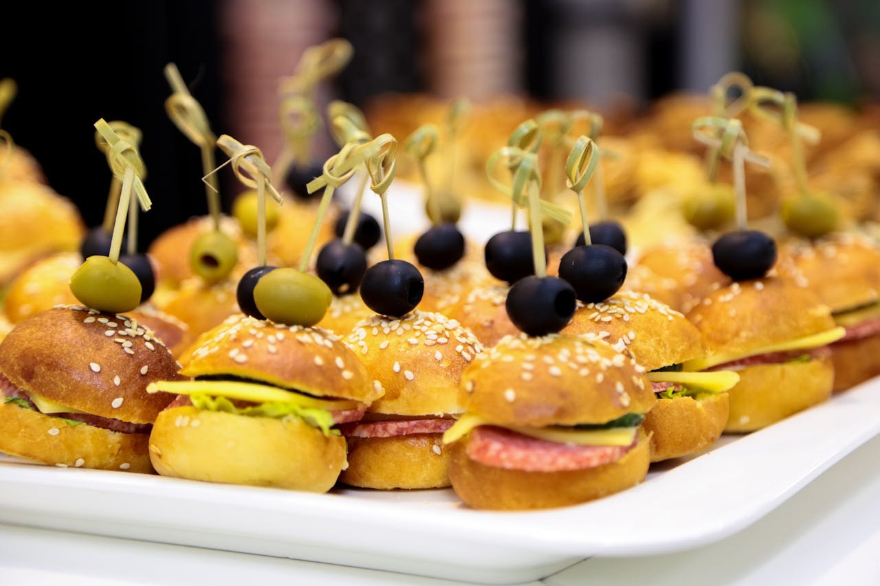 team-02 A tray of gourmet mini burgers topped with green and black olives, perfect for catering events.