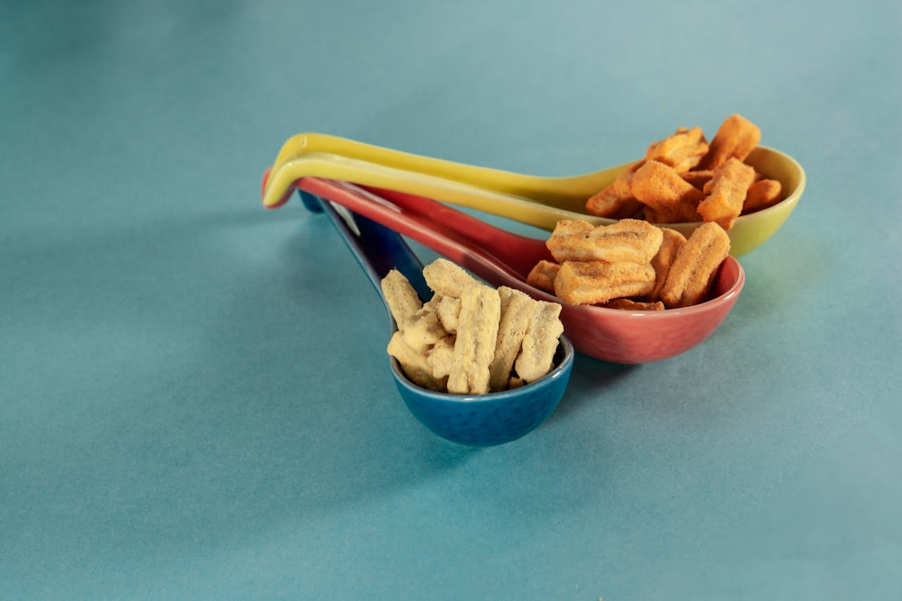 Vibrant snack display with colorful spoons filled with chips on a blue background.
